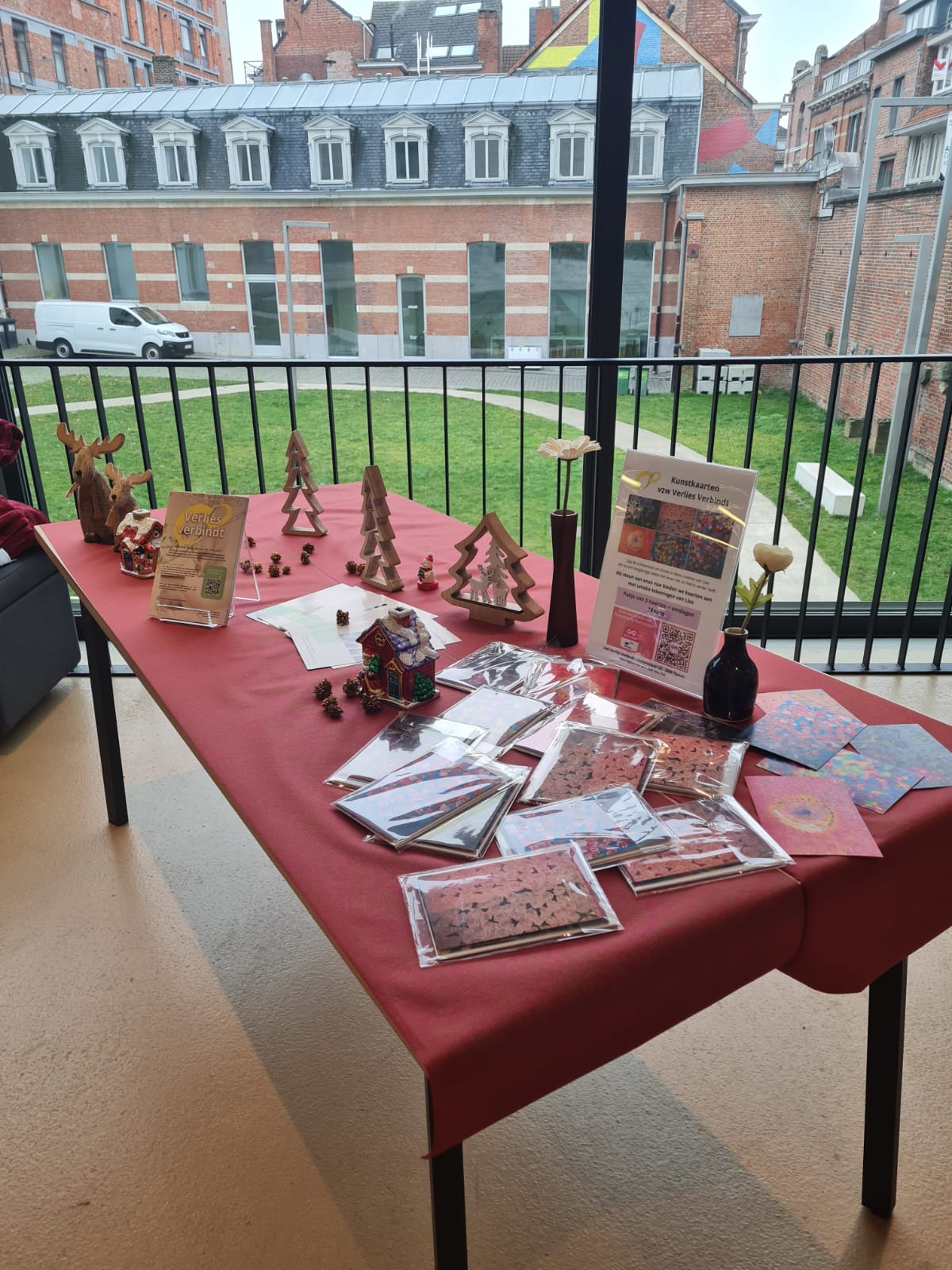 Tafel met kerstdecoraties en Lisa-kaarten, uitzicht op de binnenplaats met bakstenen gebouwen en glazen ramen.
