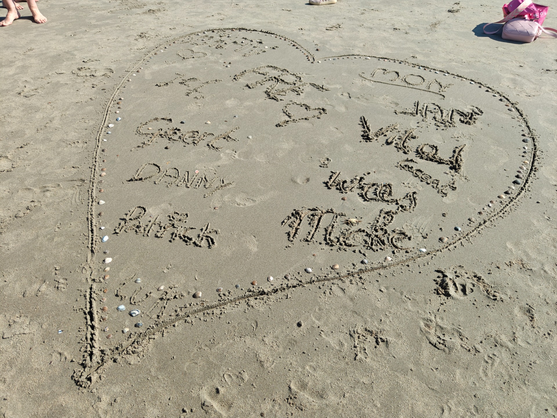 Zandcirkel met handgeschreven namen van deelnemers, op het strand.