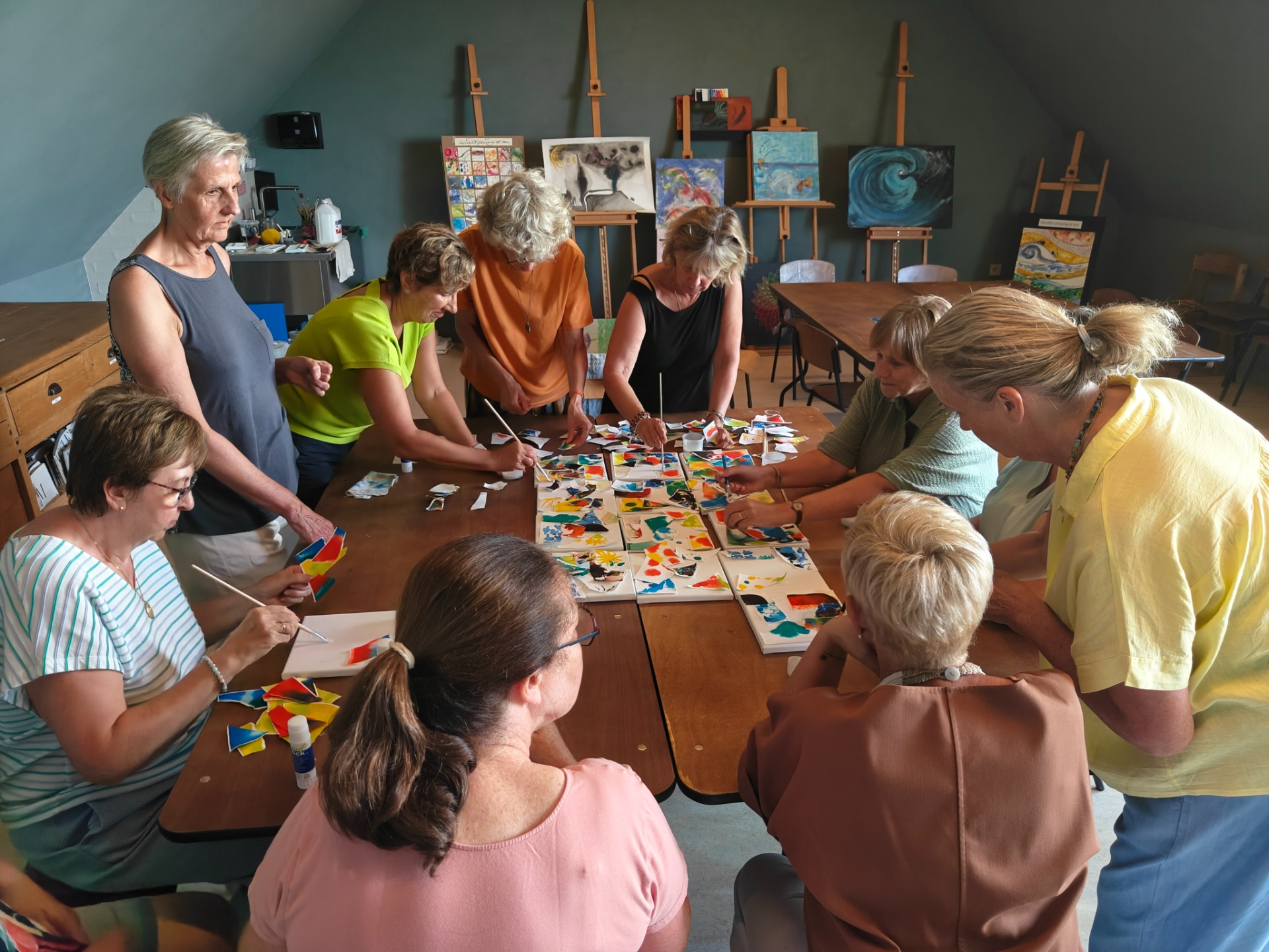 Groep mensen schildert samen aan tafel met penselen en kleurige doeken in een atelier.